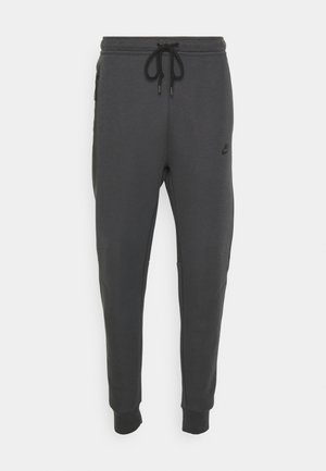 Nike mørkegrå sweatpants med tapered fit, elastisk talje, justerbar snor og sidelommer med lynlås. Blød, glat stofstruktur.