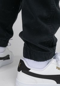 Witte sneakers met zwarte accenten en een gouden logo, met een bovenwerk van soepel leer, getextureerde overlays en een lage ontwerp.