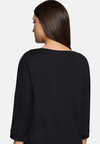 Zwart topje met driekwart mouwen, een brede halslijn en een gladde, zachte textuur. De achterkant heeft een eenvoudige naadtoevoeging.