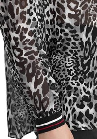 Transparante, lichte blouse met een zwarte, grijze en bruine luipaardprint. De boorden hebben een zwarte basis met witte en rode strepen.