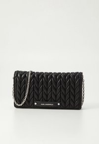 Mala tiracolo em pele preta acolchoada, com alça de corrente ao ombro e placa com logotipo. O exterior é decorado com um padrão texturizado de folhas.