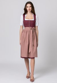 Traditionelle bayerische Tracht mit einem bordeauxfarbigen Polka-Dot-Oberteil, einer weißen Bluse und einem gefältelten rosa Rock mit feinen vertikalen Streifen und einer Schleife.