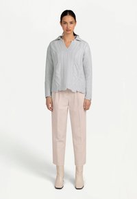 Ljusgrå stickad tröja med V-ringning och ribbad fåll, kombinerad med blekrosa byxor och beigea ankelboots, med en slät textur.