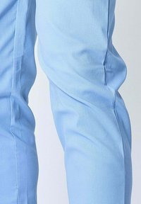 Pantalons en tissu bleu clair avec une surface texturée, présentant une coupe ajustée et un léger rétrécissement vers la cheville.