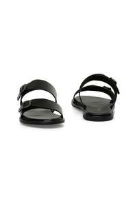 Zwarte sandalen met twee brede banden en verstelbare gespen. Platte zool met een gladde textuur. Open teenontwerp, minimalistische stijl.