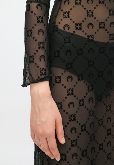 Čierne priesvitné šaty s dlhým rukávom s kvetinovými a polmesiacovými vzormi, textúrovanou látkou a volánikmi na manžetách, v kombinácii s pevným čiernym podkladom.