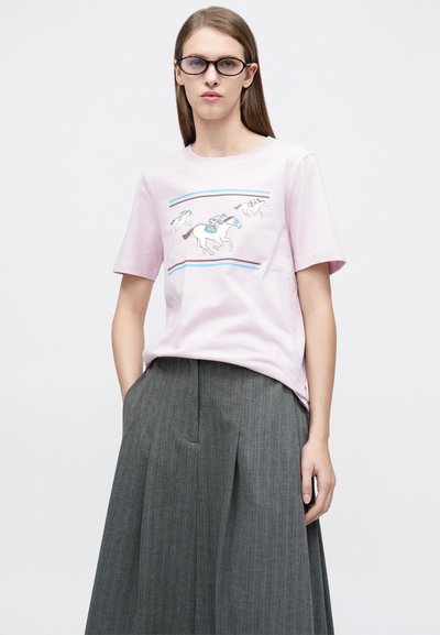 Ανοιχτό ροζ βαμβακερό μπλουζάκι με γραφικό από ιπποδρομίες και αναβάτες, συνδυασμένο με γκρι πλισέ φούστα με κάθετες ρίγες και τσέπες.