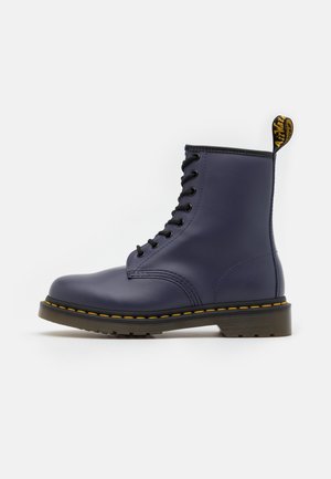 Botte en cuir bleu marine avec lacets, surpiqûres jaunes, semelle noire et languette de tirage brandée à l'arrière.
