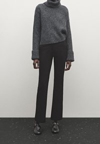 Pull à col roulé gris côtelé avec larges poignets, associé à un pantalon noir droit et des chaussures noires à détail de bride.