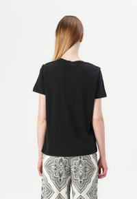 T-shirt en coton noir à manches courtes et encolure ras du cou, vu de dos, associé à un pantalon à motifs noir et blanc.