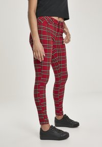Leggings à carreaux rouges avec un design ajusté, une taille élastique et des baskets noires. Présentent des accents verts et jaunes dans le motif à carreaux.