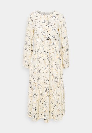 Robe crème à manches longues avec un motif de petites taches noires, bleues et orange dispersées, col rond et jupe à volants.