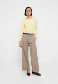 Κίτρινη μπλούζα με μακριά μανίκια, εφαρμοστή, συνδυασμένη με μπεζ παντελόνι ψηλής μέσης, φαρδιά γραμμή, δεμένο με μαύρη ζώνη, ολοκληρωμένη με σκούρα μοκασίνια.