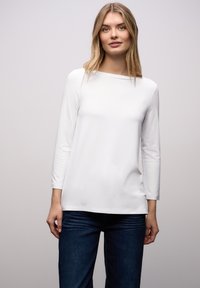 Hvid bluse med lange ærmer og b�ådudskæring; glat tekstur og afslappet pasform. Kombineret med mørkeblå jeans. Ingen synlige mønstre eller pynt.