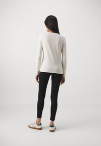 Crème lange mouwen top met een ronde hals, gecombineerd met zwarte leggings en witte sneakers met groene accenten. Minimalistisch ontwerp.