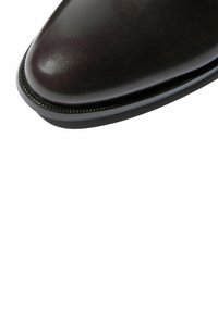 Zapato de vestir de cuero marrón con punta afilada, que presenta un acabado liso y una costura fina y texturizada a lo largo de la suela.