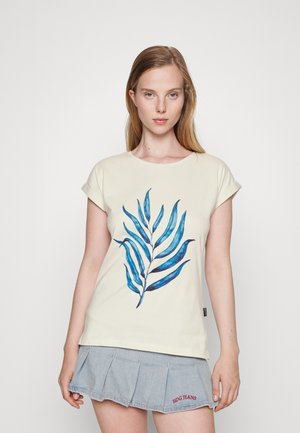 T-shirt creme com estampado gráfico de folha azul. Corte descontraído com mangas enroladas, combinado com uma saia de denim com pregas.