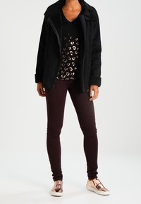 Černá zipová bunda s límcem z umělé beránkové tkaniny, spárovaná s černým topem s flitry, tmavě burgundskými legínami a růžově zlatými teniskami.