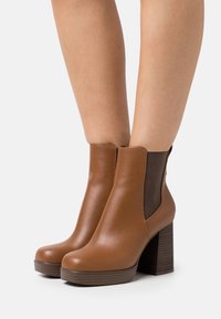 Brown leather ankle boots with a chunky heel, elastic side panels, and a smooth finish. Features rounded toes and a textured sole.
