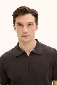 Mörkbrun pikétröja med korta ärmar och en halvvajerskrage. Tyget ser slätt och lätt strukturerat ut. Inga synliga mönster eller detaljer.