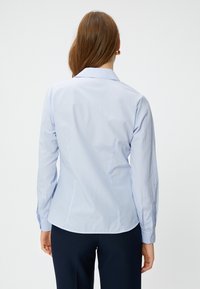 Camicia azzurra chiara a maniche lunghe con righe bianche verticali, dotata di colletto classico e polsini abbottonati, realizzata in tessuto morbido.