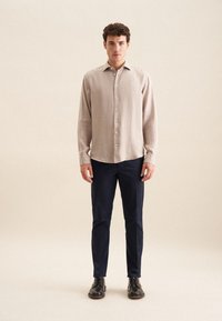 Lichtbeige linnen overhemd met knoopsluiting, een kraag en lange mouwen, gecombineerd met donkerblauwe slim-fit broek en zwarte leren schoenen.