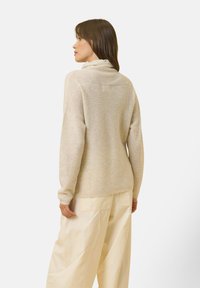 Maglione morbido e texturizzato di un beige chiaro, con colletto alto e maniche lunghe, abbinato a pantaloni crema dal taglio ampio. Design minimalista, senza motivi visibili.