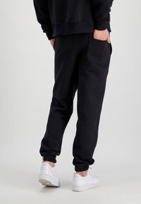 Čierne teplákové nohavice so zúženými manžetami a bočnou vreckom, kombinované s bielymi športovými topánkami. Materiál sa zdá byť mäkký a štruktúrovaný.