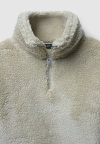 Beiger Fleece-Pullover mit hohem Kragen und halbem Reißverschluss. Verfügt über einen strukturierten, weichen Stoff mit flauschiger Oberfläche und einem kontrastierenden Innenfutter.