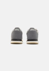 Gray ASICS sneakers featuring a smooth upper, contrasting black sole, and rounded shape, highlighting brand logo on the heel.
