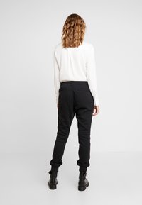 Svarta sweatpants med en tapered passform, elastisk midja och sidofickor, tillsammans med en vit långärmad tröja, sedd bakifrån.