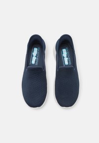 Scarpe slip-on in rete navy con suola bianca. Presentano un design flessibile, una parte superiore testurizzata e un'etichetta azzurra sulla soletta con "SKECHERS Slip-Ins."