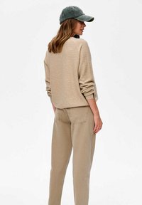 Beige gebreide trui met lange mouwen, gecombineerd met lichtbruin rechte broek. Model draagt ook een donkergroene pet.