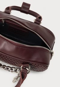 Bolsa de mão de couro vermelho escuro com fundo texturizado, fecho prateado parcialmente aberto, alça curta e cinta destacável em um fundo branco.