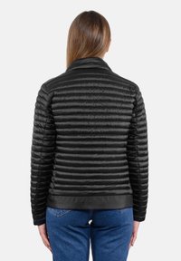 Giacca a vento trapuntata nera con colletto alto, texture a righe orizzontali e finitura liscia, indossata sopra jeans blu.
