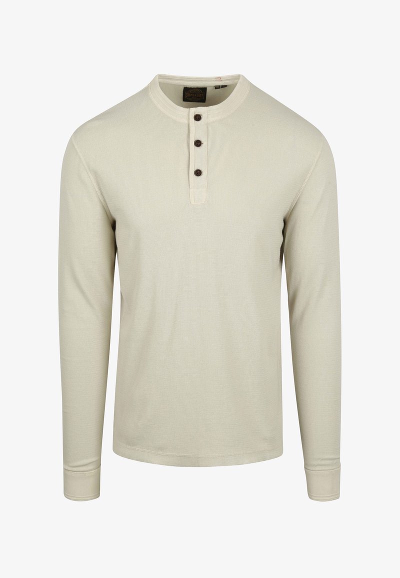 Camisa de manga larga color beige claro, hecha de algodón acanalado, con un escote redondo, tapeta con cuatro botones y puños ajustados.