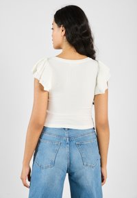 Hvit ribbet kortermet topp med volangerm, kombinert med høyt liv lyseblå jeans med baklommer og rett ben.