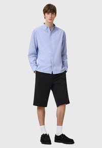 Jasnoniebieska koszula z długim rękawem, zestawiona z czarnymi szortami. Model nosi czarne buty i białe skarpetki. Prosty, casualowy design.