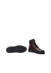 Botas de tobillo de cuero marrón con punta redonda, parte delantera con cordones y textura suave. Presentan una suela de goma plana y un cierre lateral con cremallera.