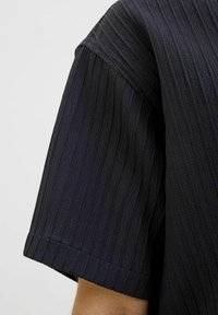 Tissu noir texturé avec des rayures verticales, conception à manches courtes et ourlet droit. Le matériau semble léger et respirant.