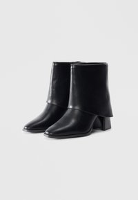 Black leather ankle boots with a folded upper, pointed toe, and chunky textured heel. Smooth finish with minimal hardware.