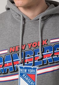 Sudadera gris con la inscripción "NEW YORK RANGERS" en letras negritas, en rojo y azul, con el logotipo del equipo y detalles de cordones.