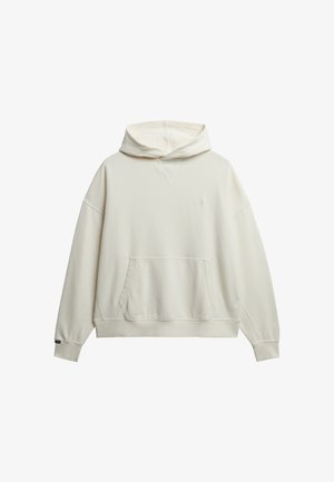 Cremefarvet hættejakke lavet af blødt stof med en stor frontlomme, brede ærmer og hætte med snor. Minimal branding på brystet.