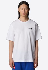 Camiseta blanca de cuello redondo hecha de algodón, con un pequeño logotipo negro en el lado izquierdo y mangas cortas. Textura suave, corte relajado.