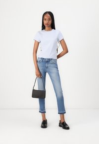 Bjela pamučna majica, svijetloplave uske traperice s izribanim rubovima i crne kožne mokasine. Mala crna torbica s remenom.