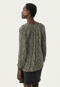 Blommig blus med svart bakgrund och gröna samt gula paisleymönster, rynkad halsringning och långa, luftiga ärmar.