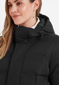 Black puffer jacket with a high collar, adjustable hood, and quilted texture. Features concealed pockets and minimalistic design.