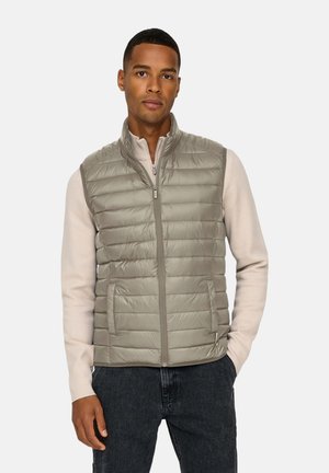 Leichte graue gesteppte Weste mit vertikalen Nähten, hohem Kragen und Reißverschluss vorne. Getragen über einem beigefarbenen Langarmshirt mit eng anliegenden Ärmeln.