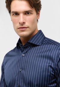 Camicia a strisce blu navy con colletto abbottonato, caratterizzata da sottili strisce verticali bianche e un tessuto liscio e strutturato.
