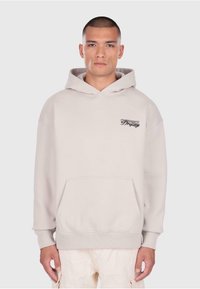 Jasnokremowa bluza z kapturem uszyta z miękkiego materiału, z przednią kieszenią, kapturem ze sznurkiem i małym czarnym logo na lewej piersi.